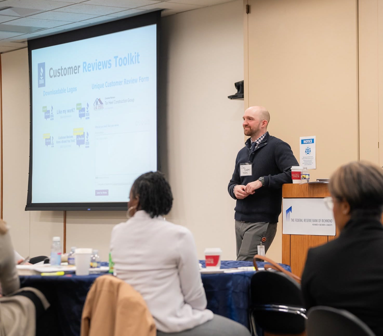 Clay presenting the Customer Reviews Toolkit, with the toolkit's sample review logos on screen and the audience seated at tables in the foreground.