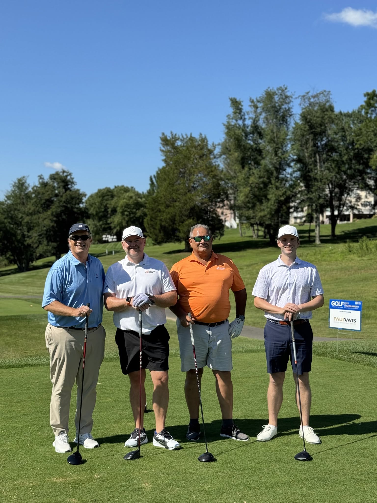 Four golfers on the course, posing beside the Paul Davis title sponsor sign.