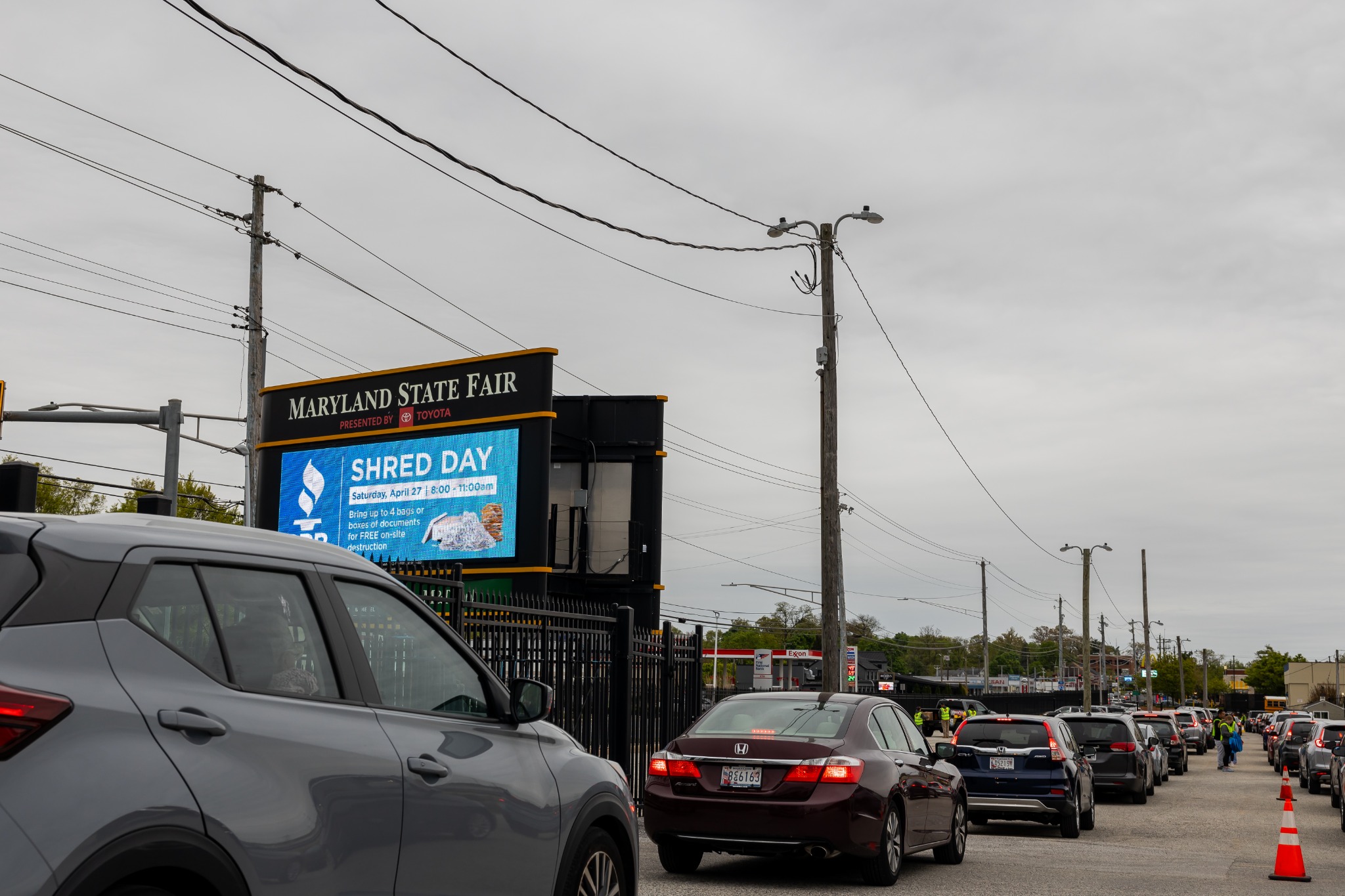 A long line of cars waiting between traffic cones past the Shred Day sign at the Maryland State Fairgrounds.